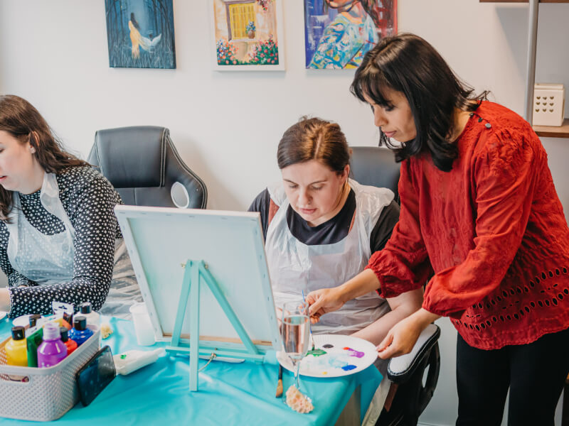 A teacher guides a student in a painting class.